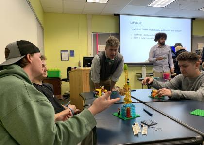 Associate Professor Michael Tews stands next to table of students creating structures with Lego blocks