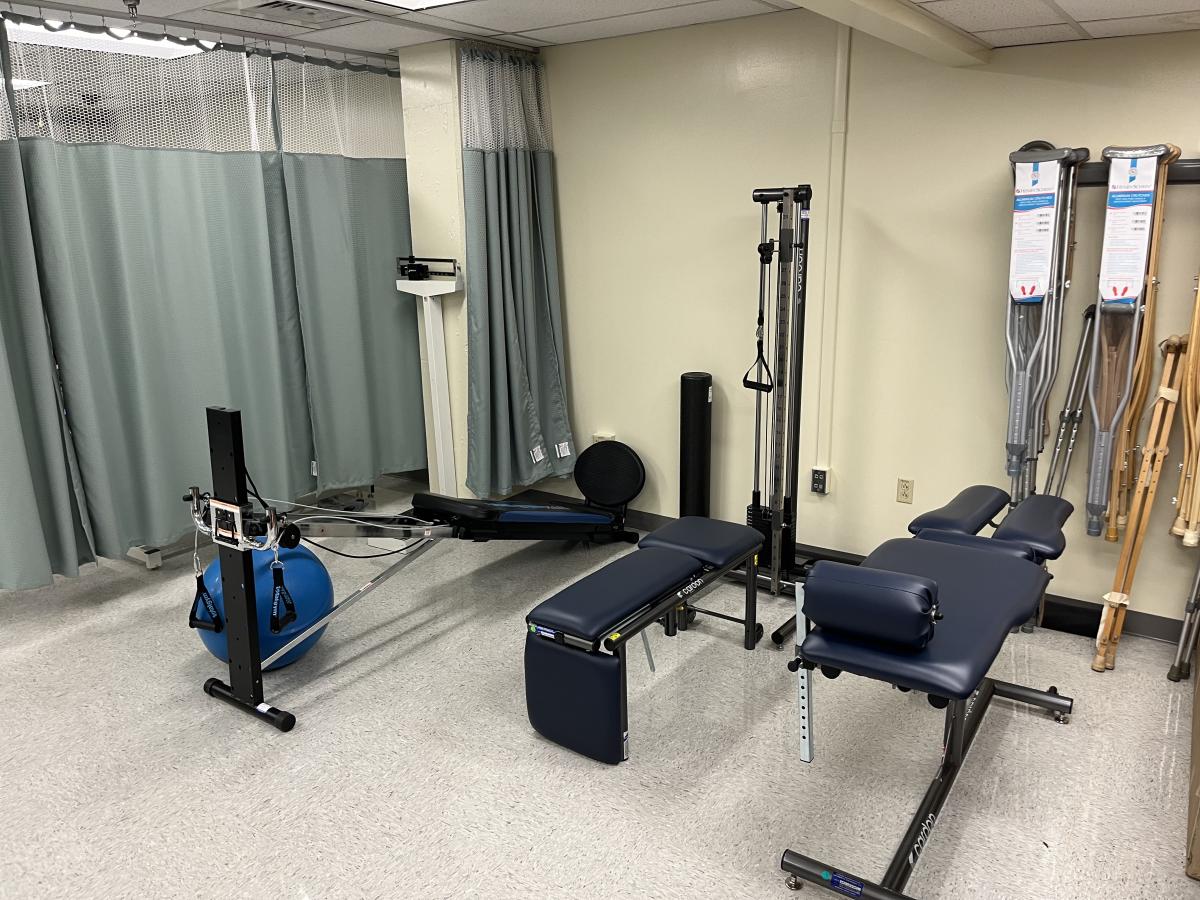 =Image depicts three pieces of athletic training equipment, an exercise ball, and various crutches hanging on the wall. There are green hospital curtains in the background.