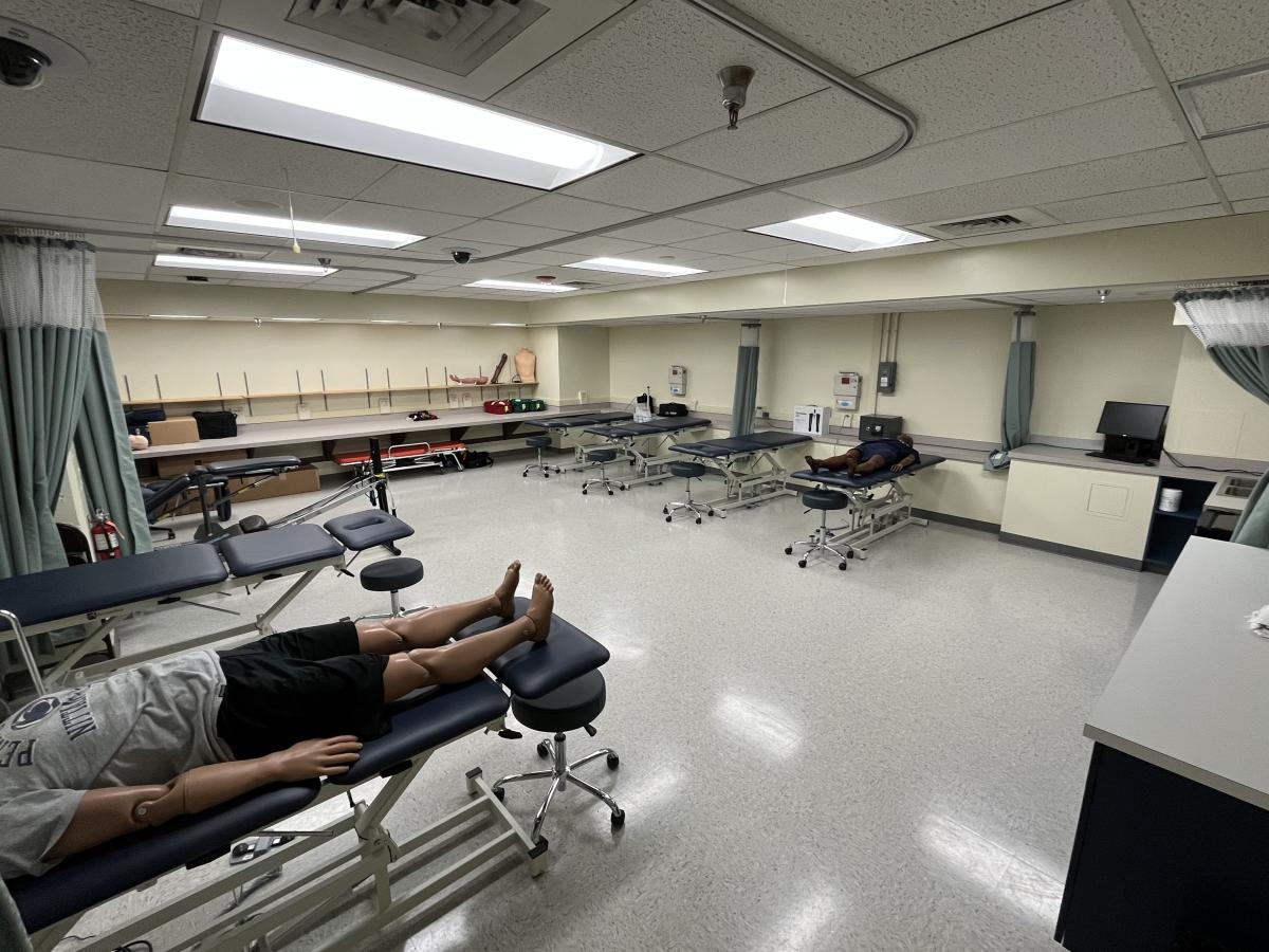=The Clinic Room features high-low tables, privacy curtains, and a medical manikin on a table. 