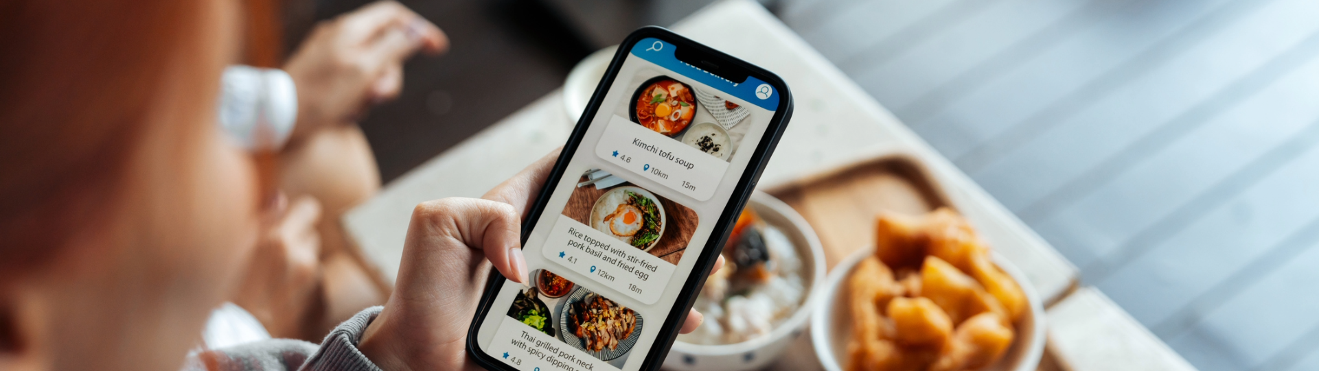 A man holds a phone looking at food ads with kids in the background.