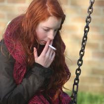 A girl smoking on a swing set.