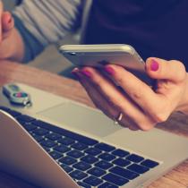 Generic Stock Photo of Woman Holding Phone with Laptop Open