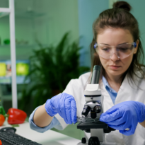 A woman wears a lab coat and places a slide on a microscope. 
