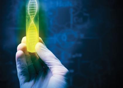 A gloved hand holding a green and yellow test tube with a DNA graphic inside on a dark background.