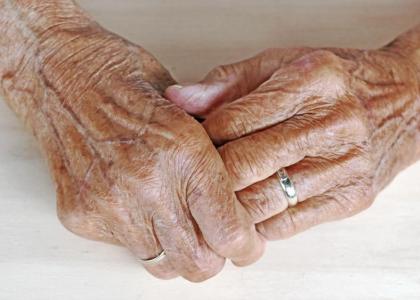 Two elderly hands clasped and resting on a table