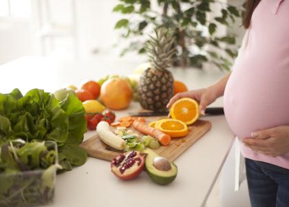 Torso of a pregnant woman in front of counter with an array of fresh fruits and vegetables