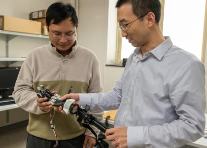 Two individuals look down at a robotic arm.