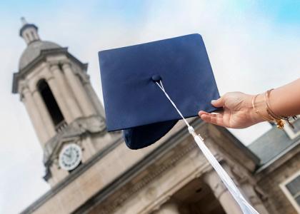 A hand holding a graduation cap in front of Old Main