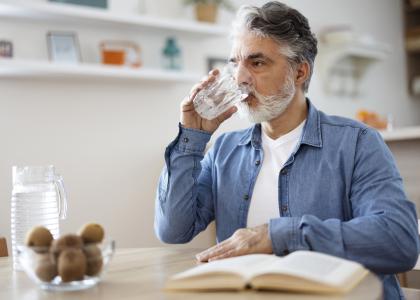 Older person sitting in a kitchen drinking water