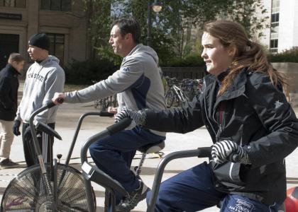 A man and a woman ride stationary bicycles outdoors on University Park campus.