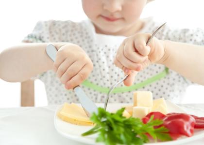 A young child using a knife and fork to eat a plate of vegetables