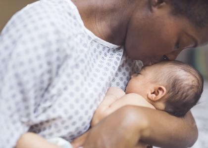 Mother wearing hospital gown kisses newborn gently on the head