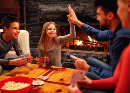 family of four playing cards in front of the fireplace, daughter gives father a high-five