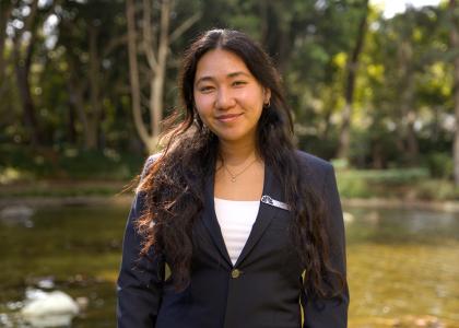 Jamie Nguyen smiles in a navy blazer standing in front of a pond and trees.