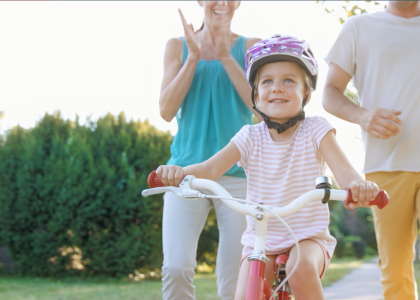 Happy child rides bike while parents watch in the background