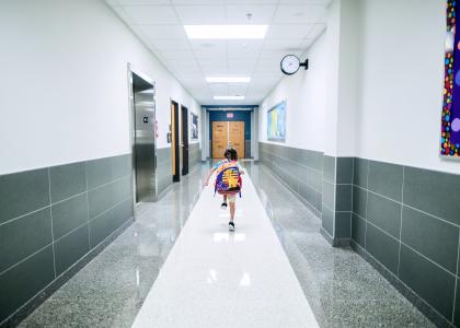 Child with backpack walking down a hallway at a school.