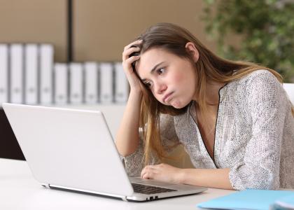 A teen girl sitting in front of a laptop with her head resting on her hand