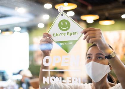 Woman in white mask hanging Open sign in restaurant window