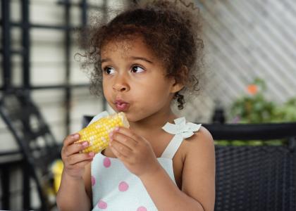 A young preschool-age girl eating corn on the cob