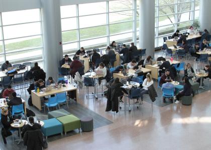 A shot from above of students sitting at tables in the Business Building Atrium.