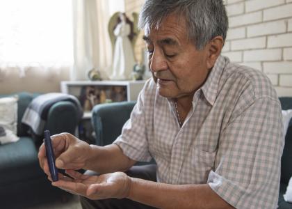 Older Hispanic man sticks his finger to test his blood sugar