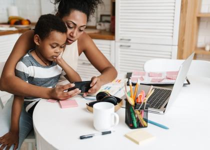 Black mother and son using mobile phone while sitting together at home