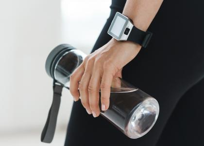 A hand wearing a Smartwatch and holding a water bottle