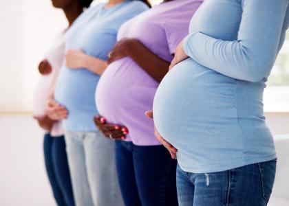 Four pregnant women in a line wearing casual clothes, shown from mid-thigh to neck