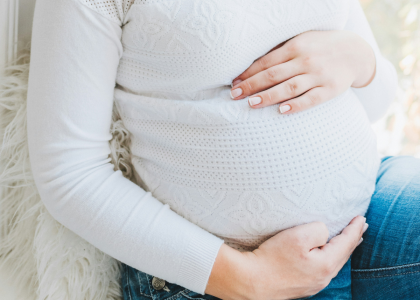 A pregnant woman in a white sweater rubbing her stomach
