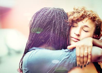 A Black woman hugs and supports a white woman