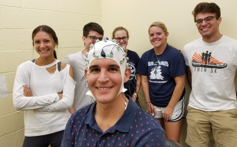 Student in foreground wears EEG cap with research team standing behind