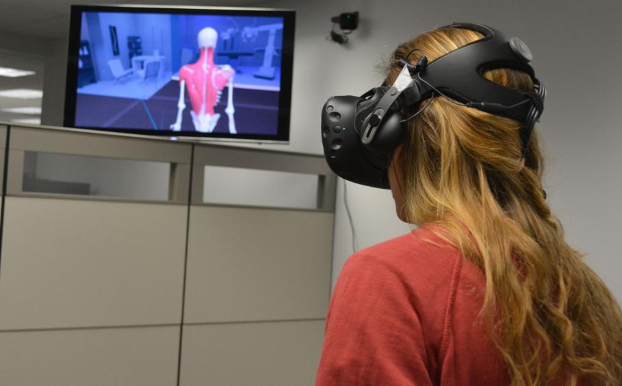 Woman in VR headset in front of screen that shows muscle groups on human back