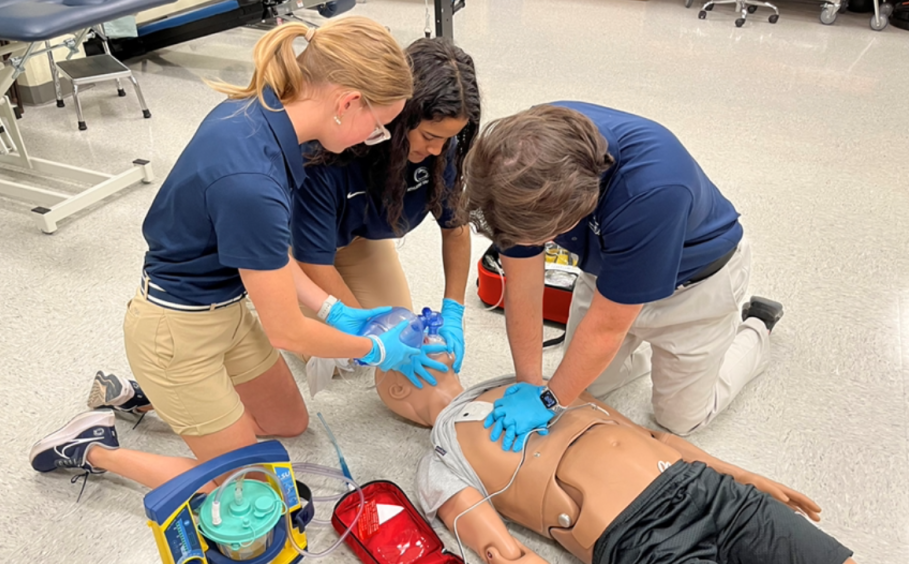 Three students practice administering CPR to a medical manikin. 