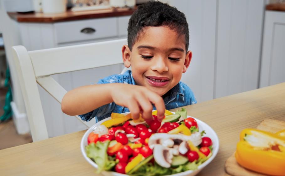 child happily chooses from a bowl of vegetables
