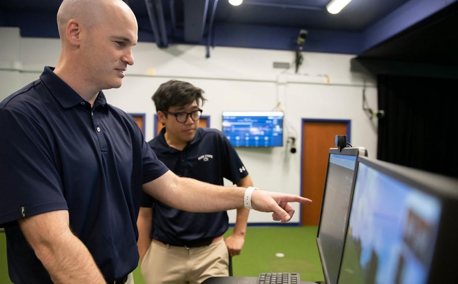 Instructor reviewing data with with PGM student in the A image of two instructors working with a golfer in the Golf Teaching and Research Center.