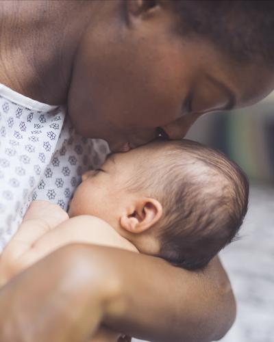 Mother in hospital gown kissing newborn on the head