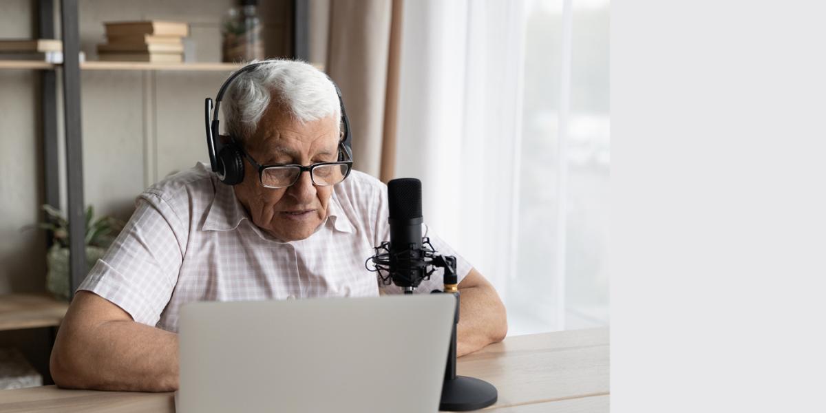 elderly man sitting at desk with laptop and microphone