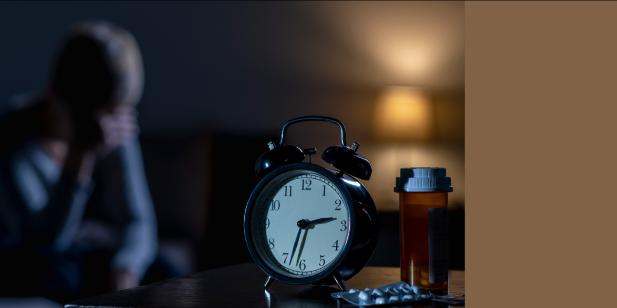 Woman sitting awake in her bed next to an alarm clock and pill bottle
