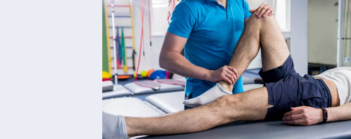 A physical therapist helps a patient stretch their leg on a therapy table.