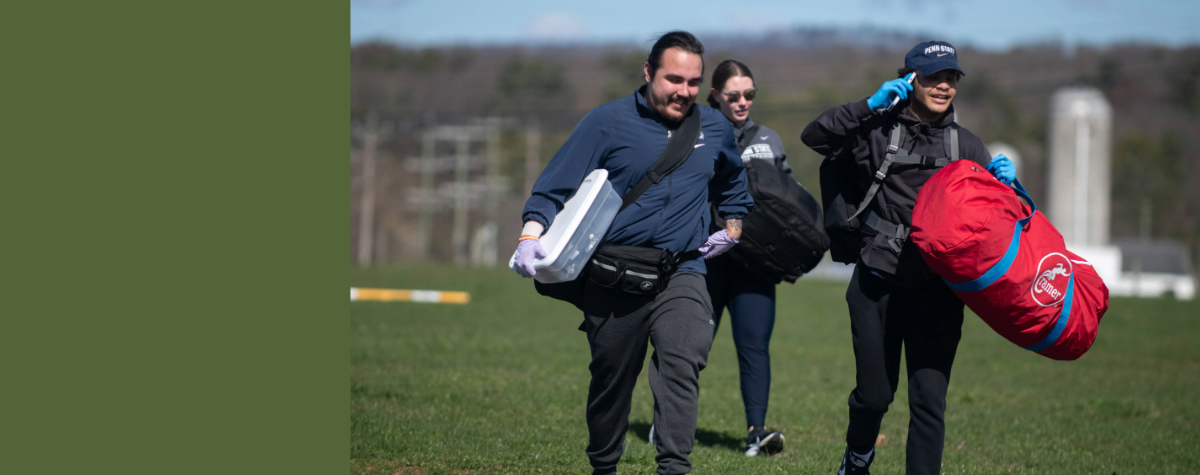 Athletic training students walk across a grassy field carrying emergency equiptment.