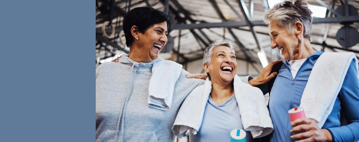 Three older women stand together laughing after a gym class. 