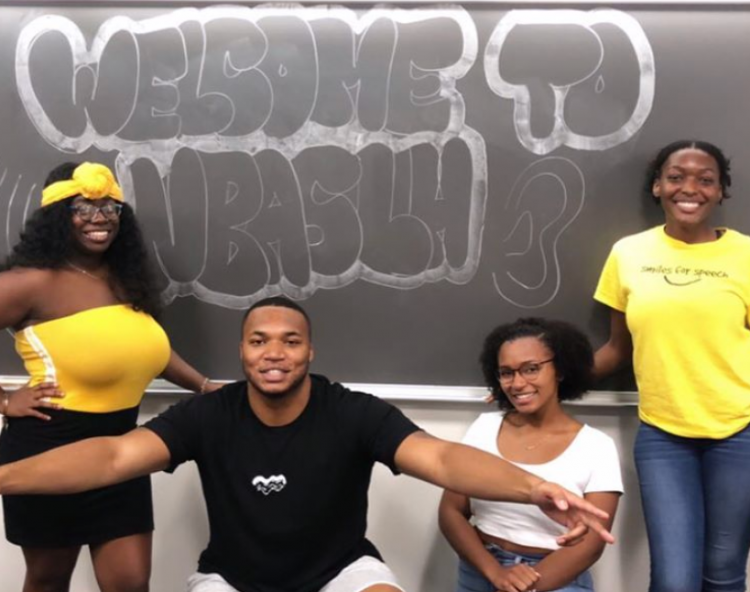 Four students posed in front for chalkboard with welcome written on the board.