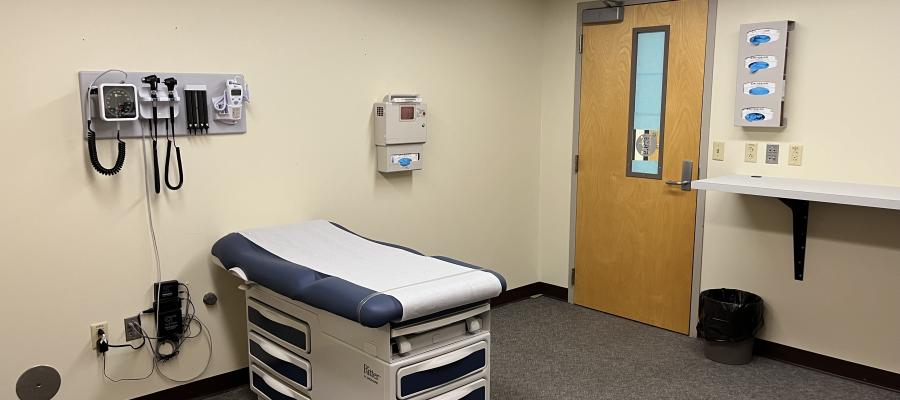 This exam room has a treatment table, like you would see in a doctor's office, with the wall containing healthcare equipment such as a thermometer and a blood pressure cuff.