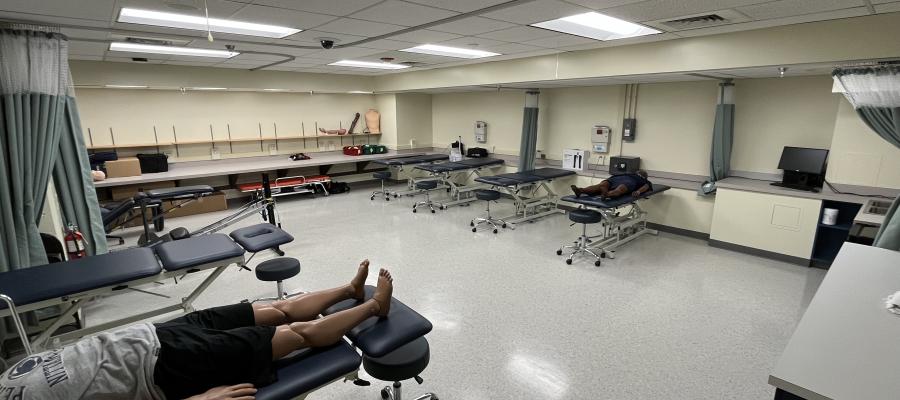The Clinic Room features high-low tables, privacy curtains, and a medical manikin on a table. 
