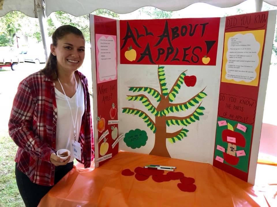 =Ellie Manca, a BBH student and SNAP-Ed Student Project Assistant, stands with her interactive apple poster at the CenClear Fall Festival.