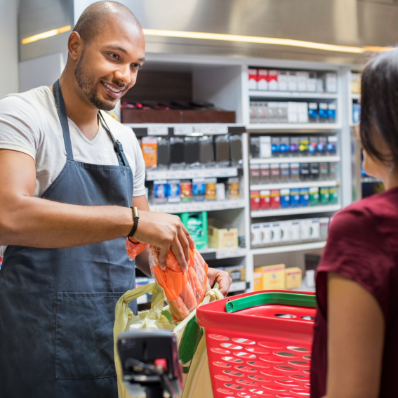  A man works as a cashier bagging groceries for a woman.
